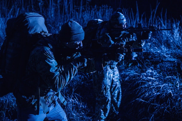 Two soldiers, special forces fighters, border guards team, counter-terrorism tactical group shooters aiming rifles, stopping offenders, attacking enemies during night patrolling, at sabotage mission