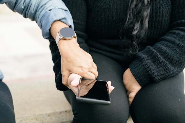 two spanish-latin women with smartphones and smartwatches selective focus on the clipped hands