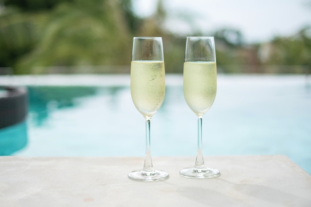 Two sparkling champagne glasses or prosecco near swimming pool