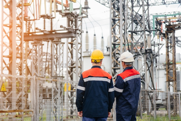 2人の専門の変電所エンジニアが日没時に現代の高電圧機器を検査します。エネルギー。業界。