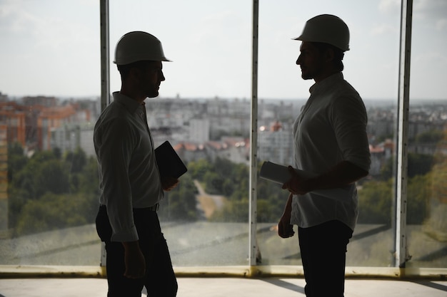 Two specialists inspect commercial industrial building\
construction site real estate project with civil engineer