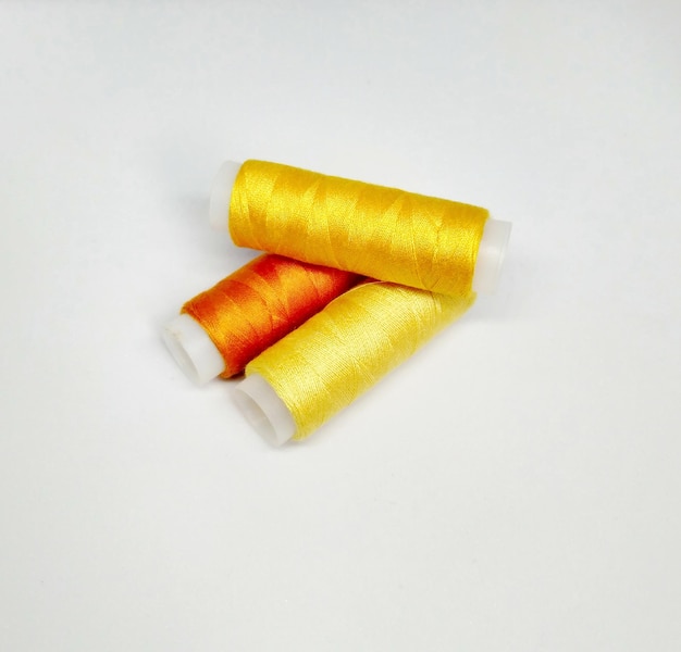 Two spools of yellow thread with a red thread on a white background.