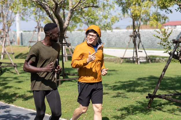 Photo two sport people black man and asian man jogging and running together in park at autumn morning.