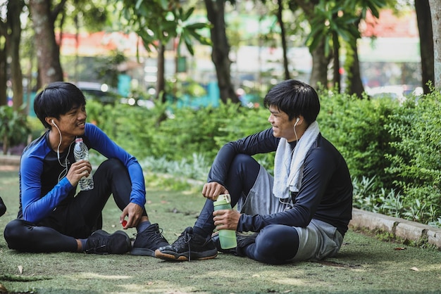 Two sportmen in sportswear talking and drinking water together on the ground while resting after wo