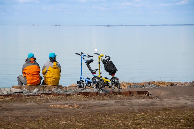 Two sporty fullyequipped cyclists sitting on a shore with bikes and looking at the landscape and sea