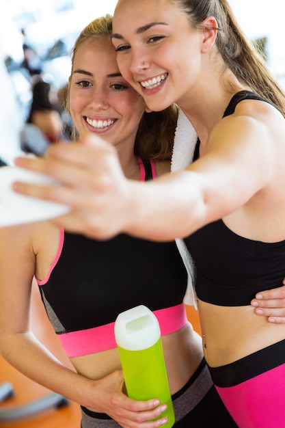 Two sporty young woman using mobile phone in gym.