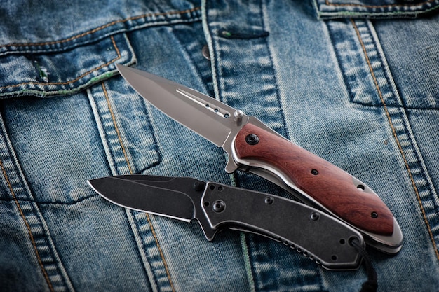 Two stainless steel folding knifes over denim jacket