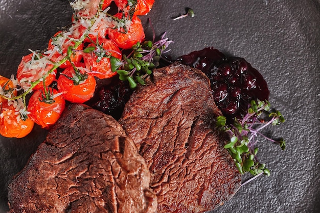 two steaks on a dark plate with sauce and cherry tomatoes on a dark background banner