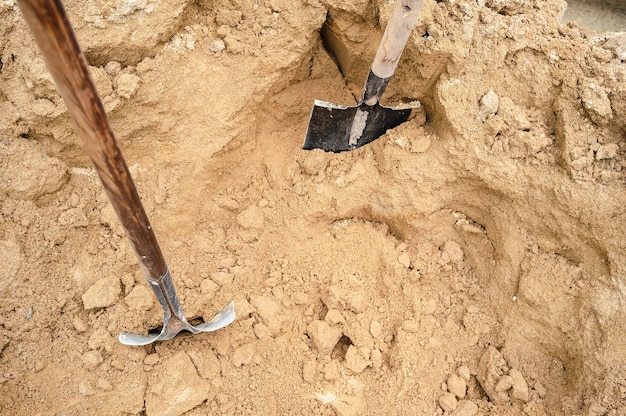 Фото Две стальные лопаты с деревянными ручками в куче песка на открытом воздухе.
