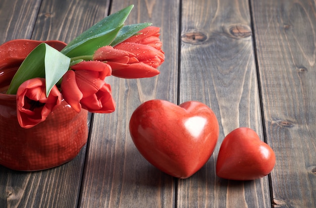 Two stone hearts and bunch of red tulips on wooden background