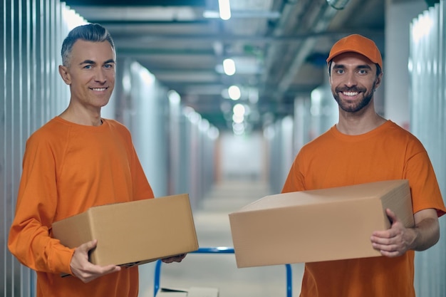 Two storehouse loaders holding cardboard boxes and looking ahead