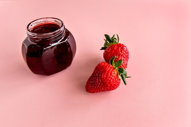 Photo two strawberries and strawberry jam on pink background