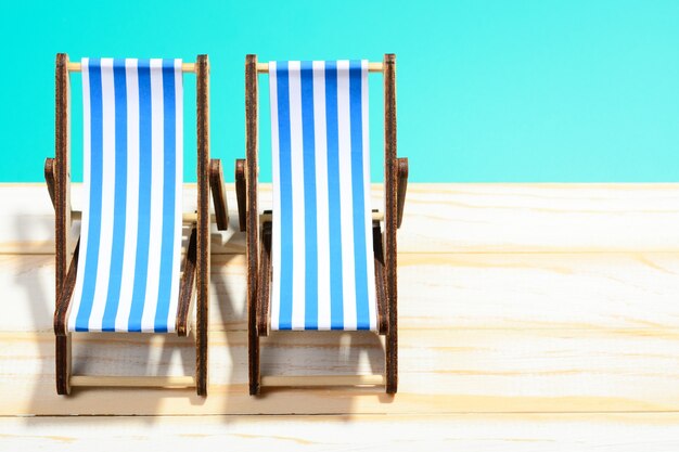 Two striped beach chairs on wooden surface and blue background