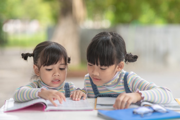 テーブルの上の本を読んでいる2人の学生の小さなアジアの女の子