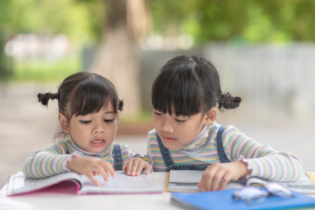 Two student little Asian girls reading the book on table