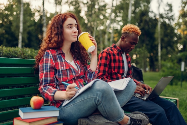 Two students drinks coffee on the bench in park