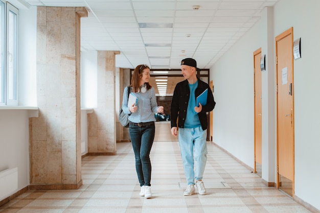 Two students a guy and a girl are walking along the corridor of the university and discussing educational material