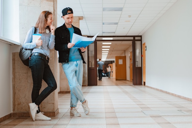 Two students a guy and a girl are walking along the corridor of the university and discussing educational material