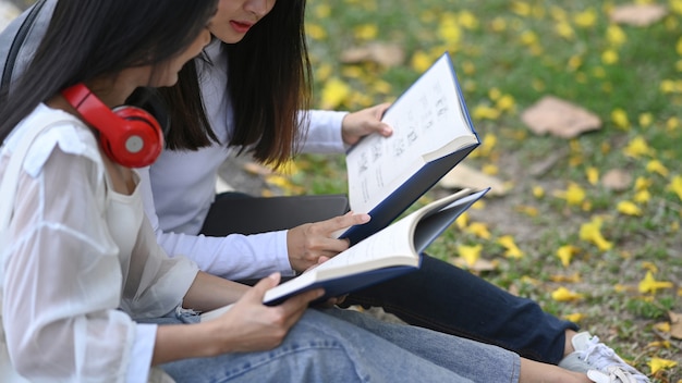 Two students  holding book and talking about lessons comparing together in the campus.