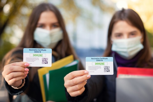 Two students showing vaccination certificates cards to the camera focus on certicites