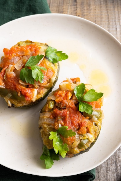 Two stuffed zucchini boats on a plate with a wooden table in the background.