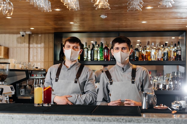 Фото Два стильных бармена в масках и униформе готовят коктейли на вечеринке во время пандемии работа ресторанов и кафе во время пандемии