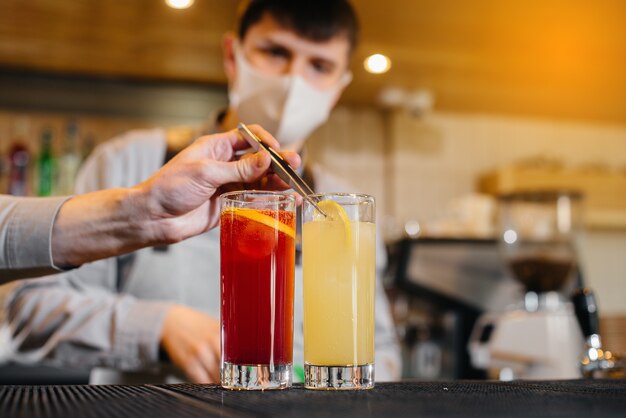 Two stylish bartenders in masks and uniforms during the pandemic, preparing cocktails. The work of restaurants and cafes during the pandemic.