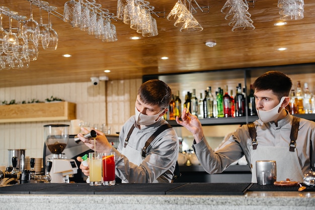 Two stylish bartenders in masks and uniforms during the pandemic, preparing cocktails