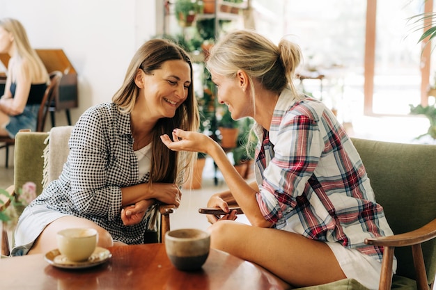 Photo two stylish female girlfriends are talking while sitting in a cafe