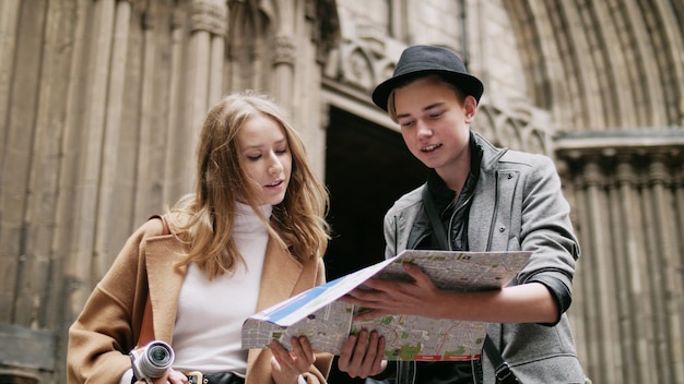 Two stylish friend standing at the street and look for something using a map. They looking around. They are speek and enjoing of joint walk.