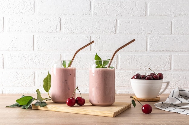 Two stylish glasses with freshly made cherry smoothies and a bowl of ripe cherries on the wooden board A delicious healthy drink Detox