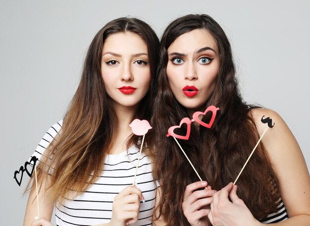 Two stylish sexy girls best friends holding paper party sticks