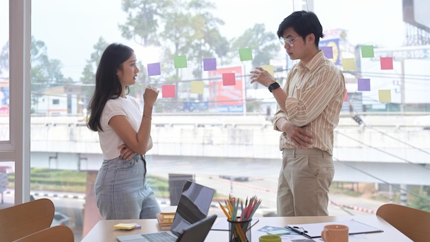 Two successful business partners discussing business plans while standing near large window at office