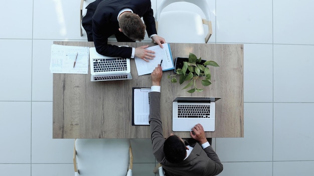Два успешных улыбающихся бизнесмена работают над ноутбуком, вид сверху