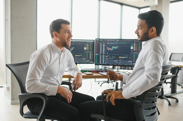 Two successful trader sitting in office and looking at screen checking cryptocurrency information data on finance market graph pointing on monitor