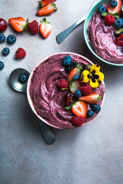 Two summer acai smoothie bowls with strawberries blueberries on gray concrete background Breakfast bowl with fruit and cereal closeup top view healthy food