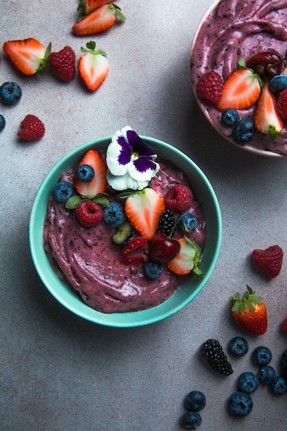 Two summer acai smoothie bowls with strawberries blueberries on gray concrete background Breakfast bowl with fruit and cereal closeup top view healthy food