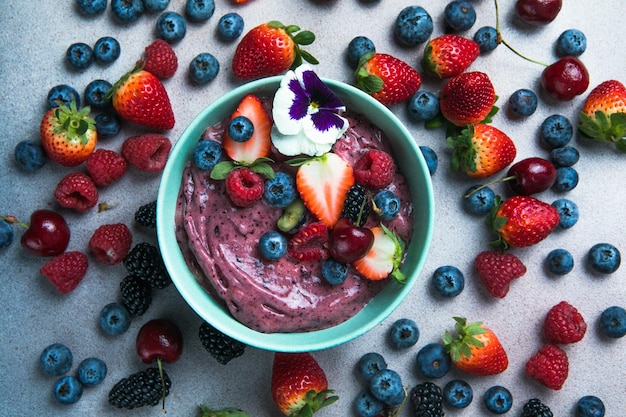 Two summer acai smoothie bowls with strawberries blueberries on gray concrete background Breakfast bowl with fruit and cereal closeup top view healthy food