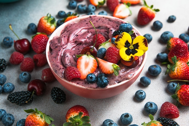 Two summer acai smoothie bowls with strawberries blueberries on gray concrete background Breakfast bowl with fruit and cereal closeup top view healthy food