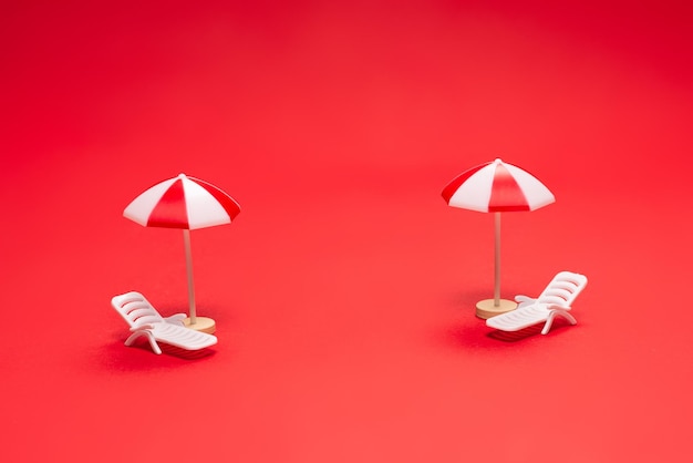 Two sun loungers and red umbrellas on a red background. Copy space.