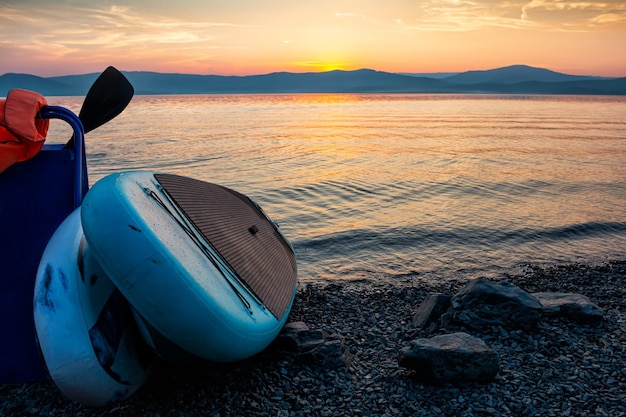 Photo two sup boards on the shore of a scenic lake against the backdrop of sunset