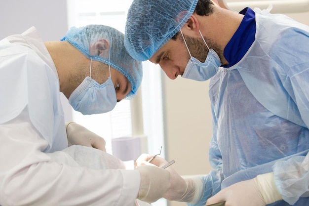Два хирурга в синих халатах делают операцию в операционной, крупным планом