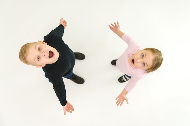 The two surprised kids stand on the white background. View from above