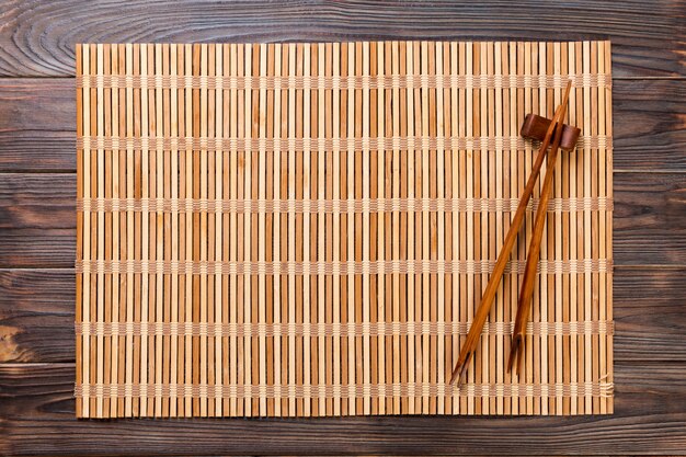 Two sushi chopsticks with empty brown bamboo mat or wood plate on wooden