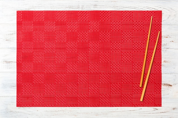 Two sushi chopsticks with empty red tablecloth, napkin on white wooden surface Top view with copy space