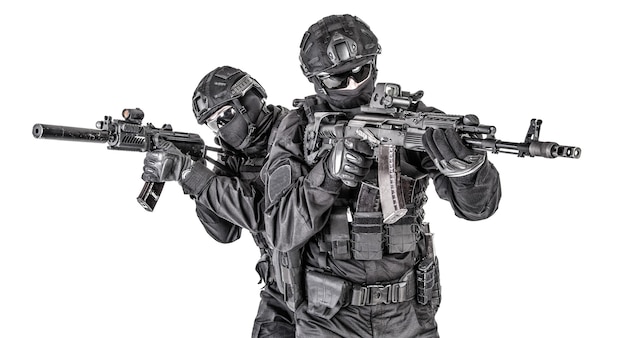 Two SWAT fighters, police special operations tactical group members in black uniform ans helmet, armed with assault rifles moving forward one behind another studio shoot isolated on white background