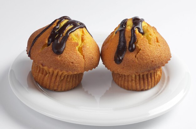 Photo two sweet cupcakes with chocolate in plate on white