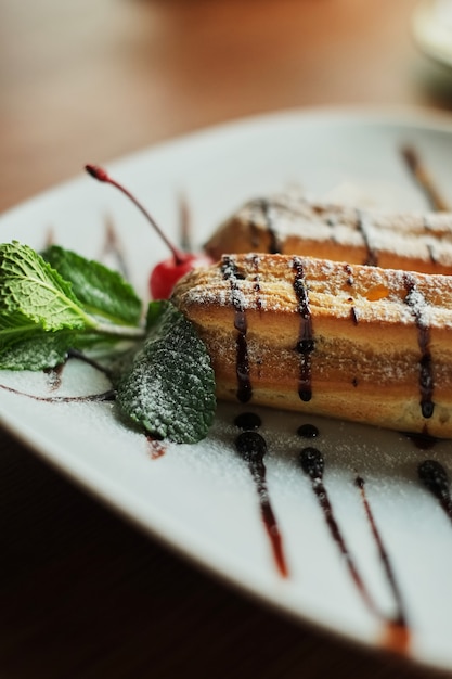 Two sweet french eclairs on plate. Breakfast in cafe. wooden table background close-up