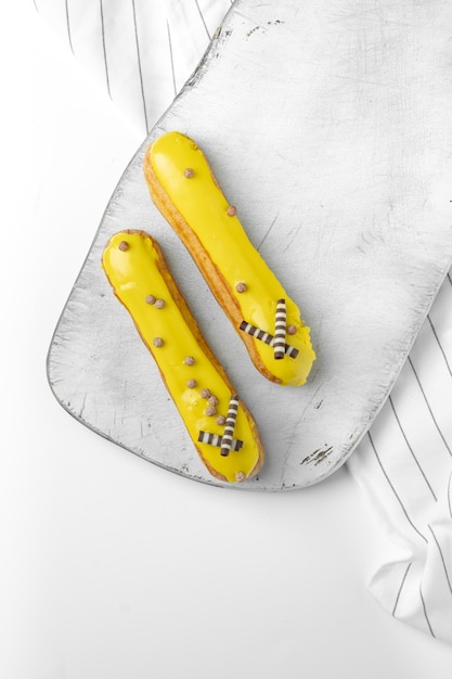 Two sweet french yellow eclairs on a white wooden Board in the kitchen, top view