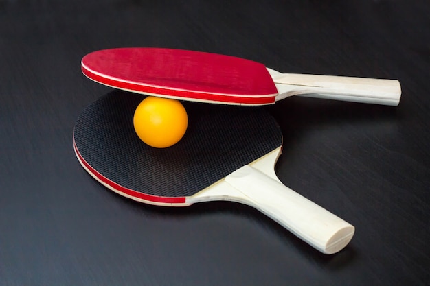 Two table tennis or ping pong rackets and ball on a black table